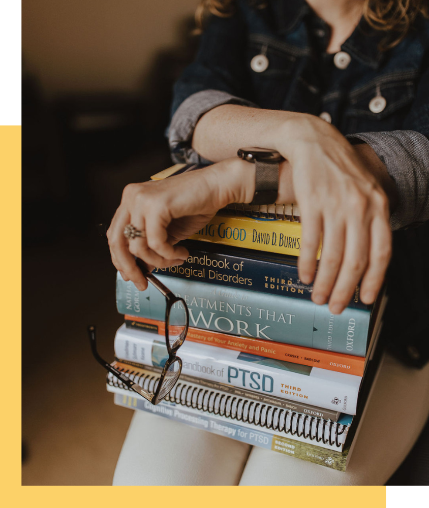 Image of a stack of books on PTSD and Anxiety with Melissa's arms crossed holding glasses.