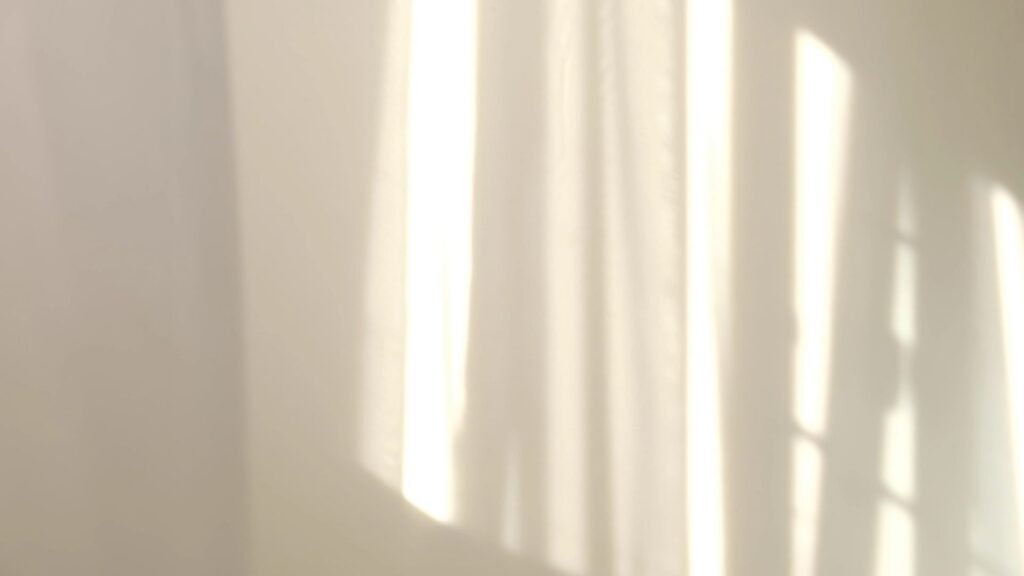 Soft, blurred sunlight streaming through a window, casting abstract shadows and light patterns on a pale wall.