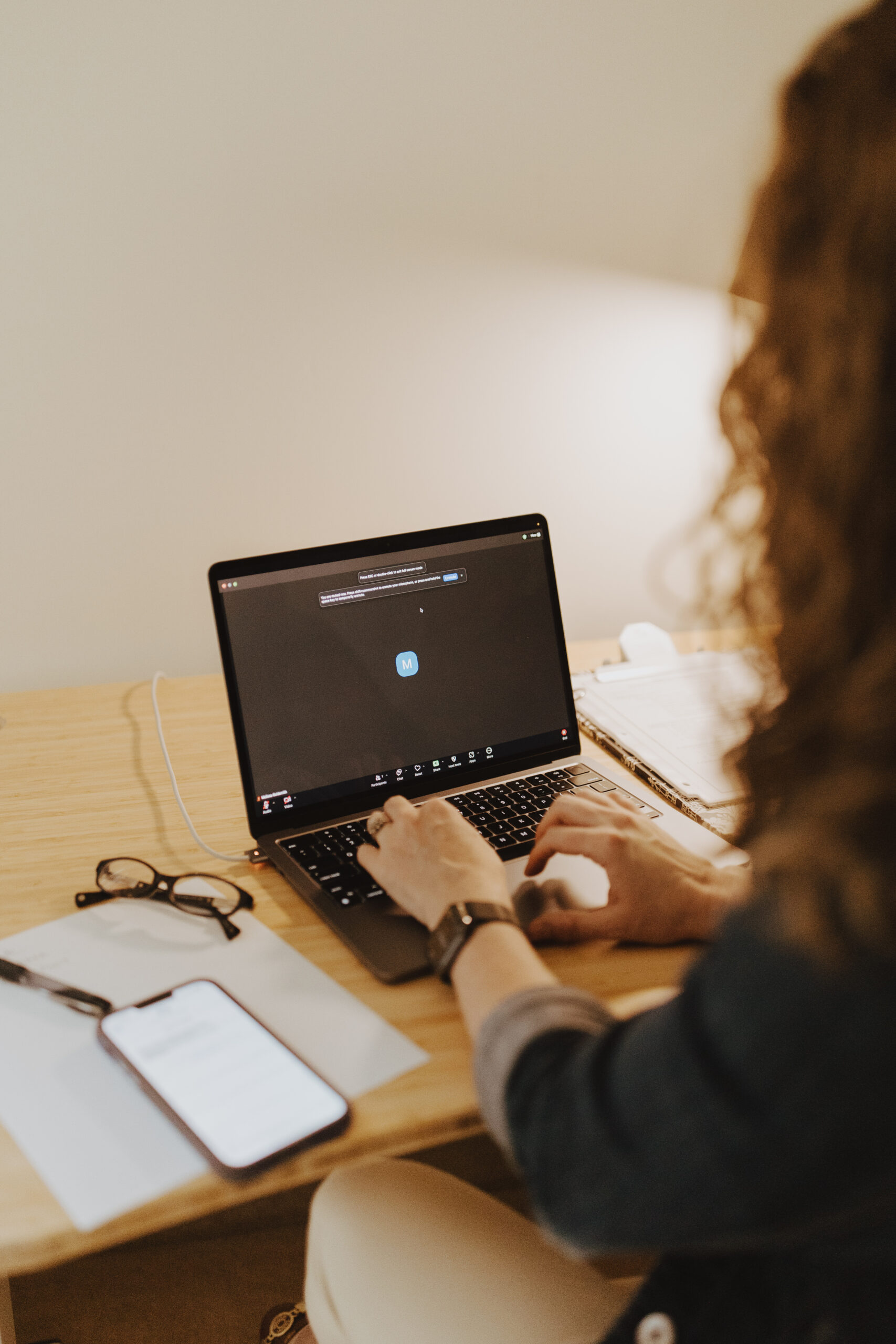 Melissa Goldsmith at her computer entering an online therapy session on a wood desk