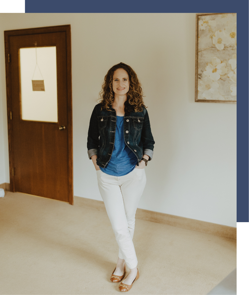 Melissa standing in her office in front of a white wall with a floral print in the background, smiling
